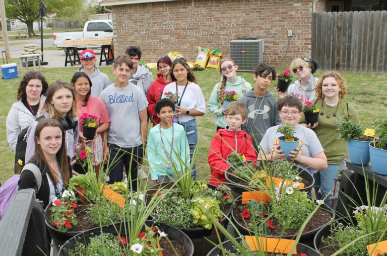 A group of students stand in front of colorful flowers in planters.